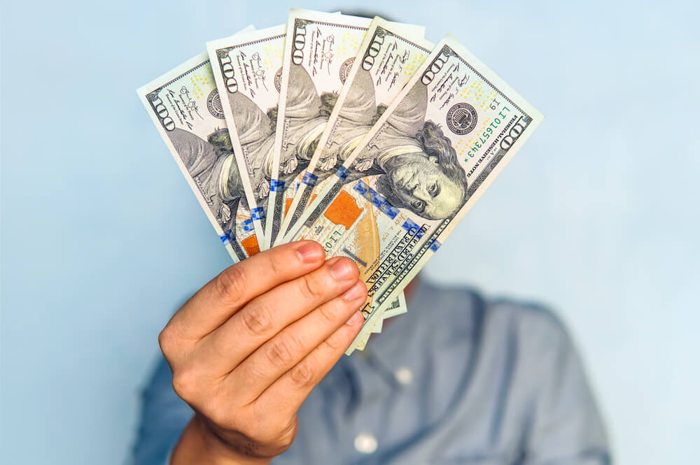 In the image, a man holds cash, symbolizing a payday loan transaction for quick financial assistance