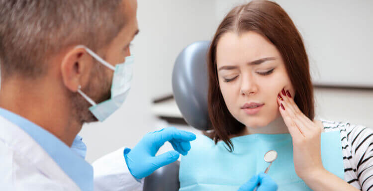 woman holding mouth from dental pain and in chair at dentist