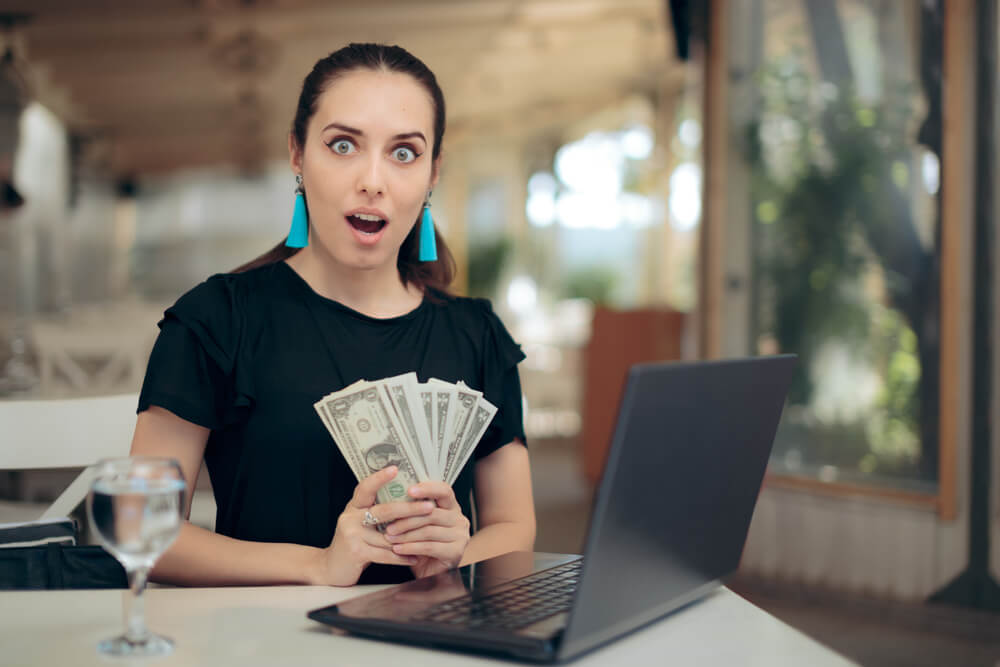 woman holds cash at the computer after getting emergency funds with 