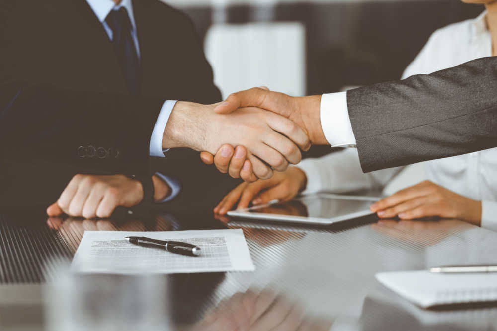 A car title loan agreement with two sides shaking hands in a room containing documents on a table.