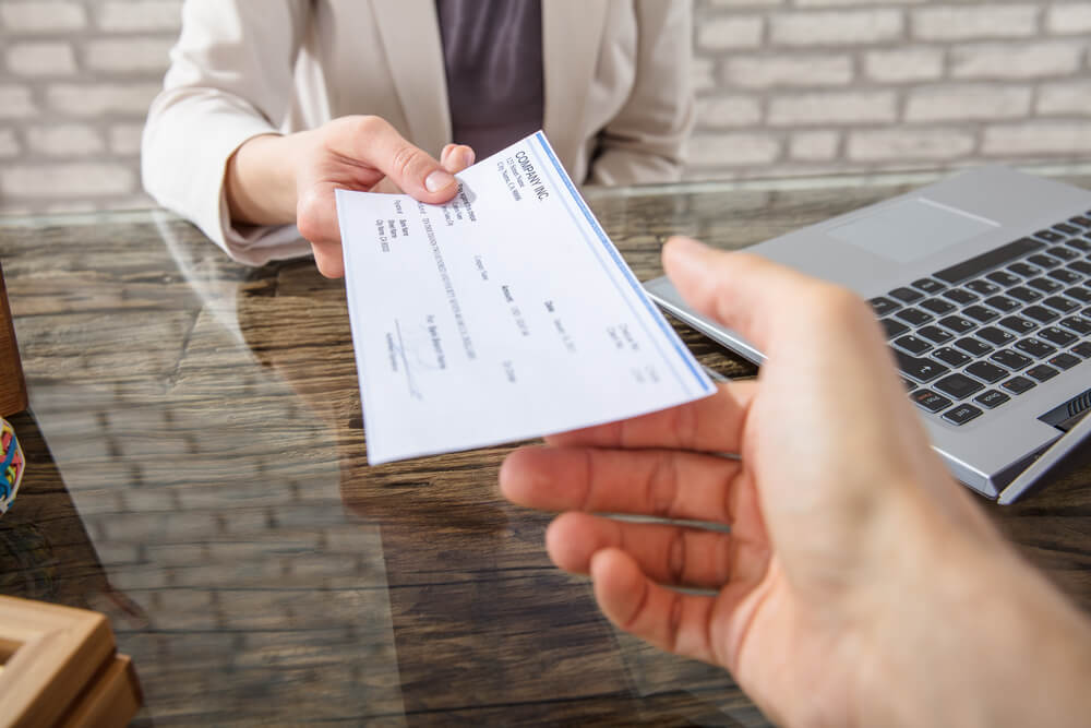 Close up of hand receiving title loan check from representative to break the paycheck to paycheck cycle