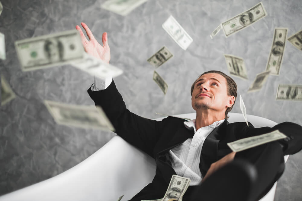 man sitting in chair with money floating around him