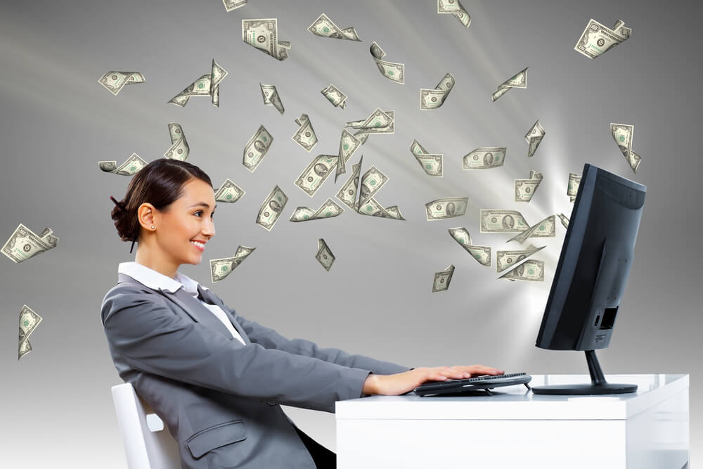 Woman sitting at her desk with title loan cash flying from the screen for symbolizing quick car title loans online 