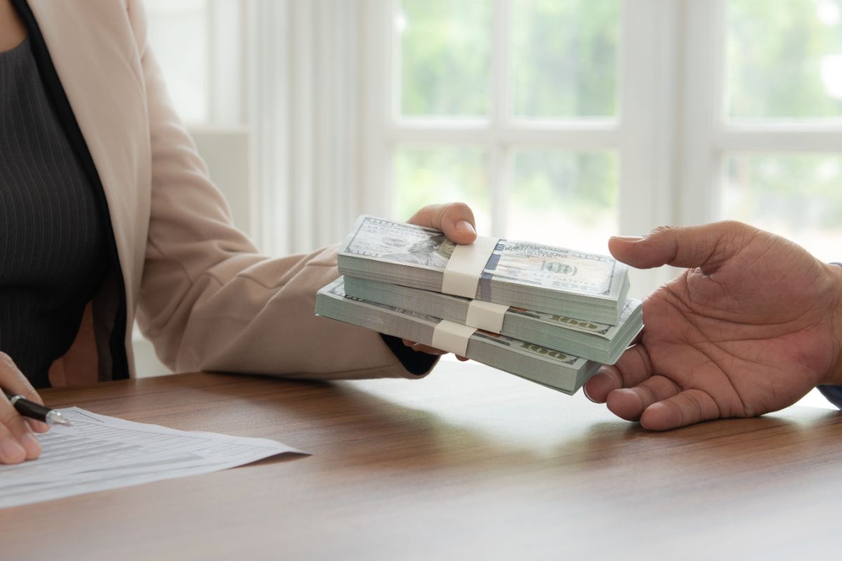 A fast cash title loan: a woman exchanging a bundle of money with a representative on top of a table and filling out paperwork.