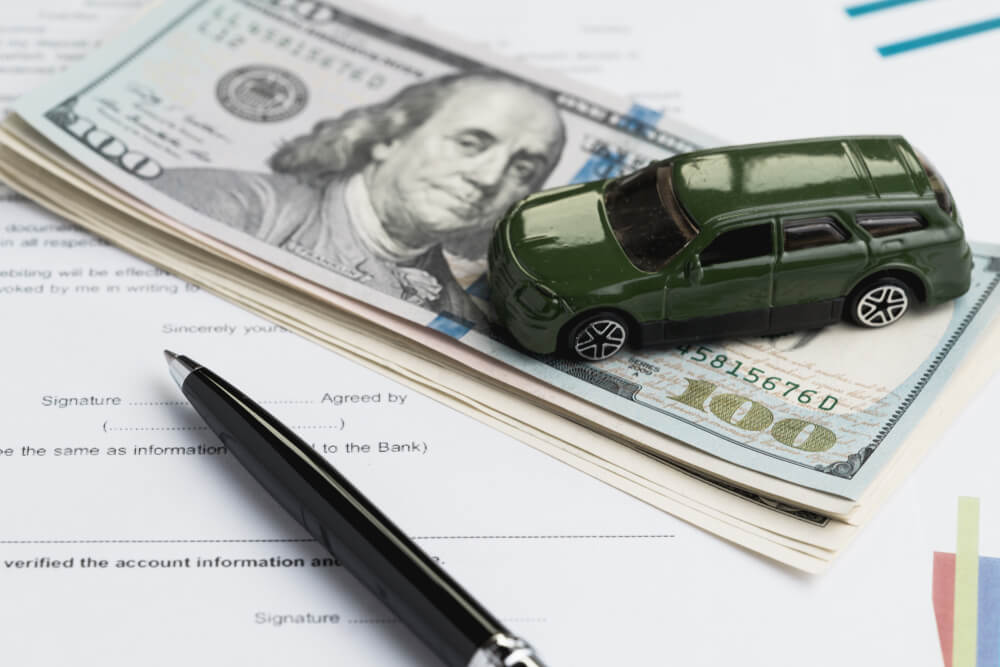 Miniature car on top of title loan cash and paperwork on a desk