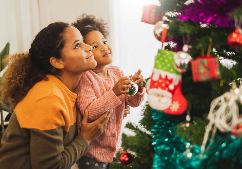  A mother and daughter follow self-care tips for the holidays by putting Christmas lights on a tree.