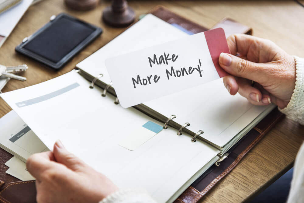 person reviewing documents and holding paper that say make more money