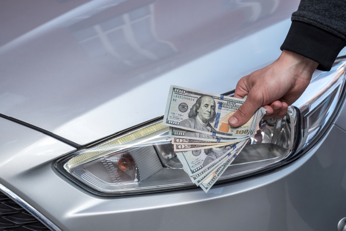 man holding title loan cash in front of his car