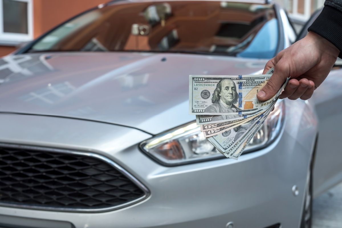 man holding title loan cash in front of their car