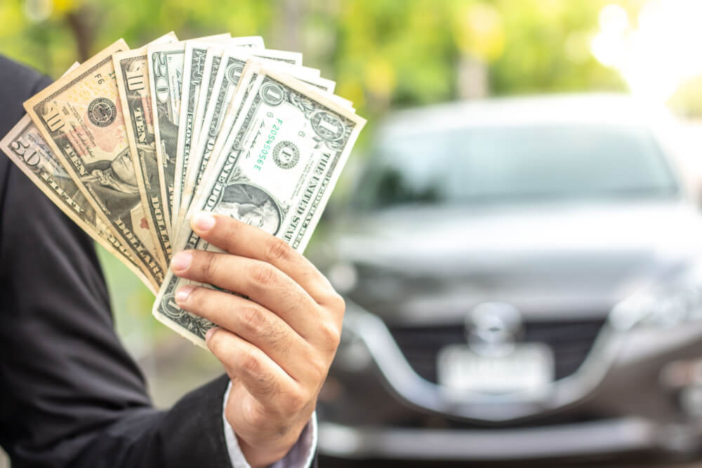 A man got a title loan holding in his hand and a background of black car on the back and trees.