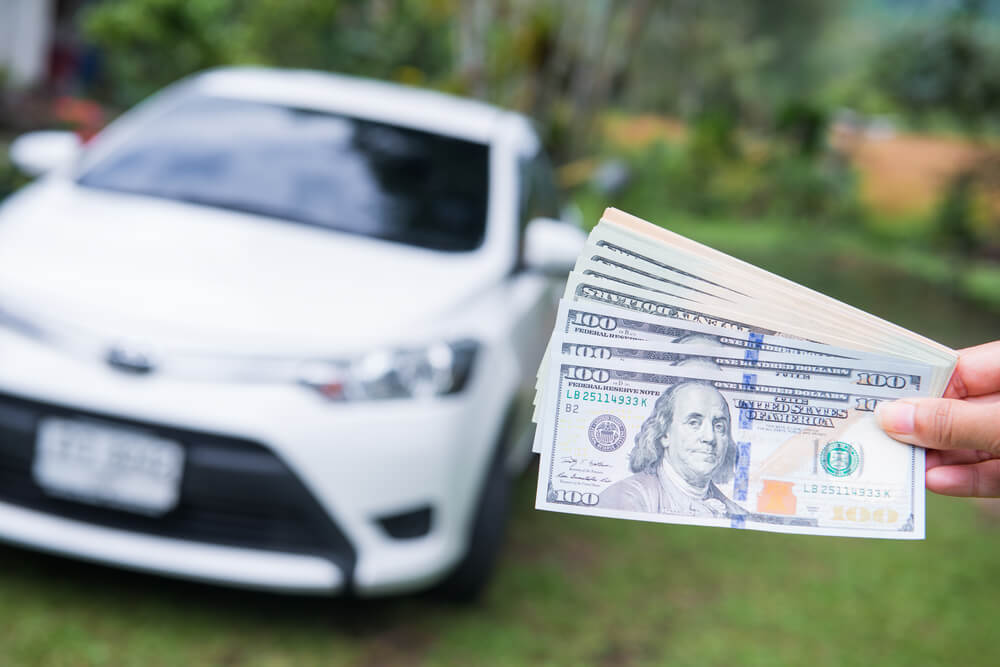 Person showing their title pawn cash in front of their car on the lawn