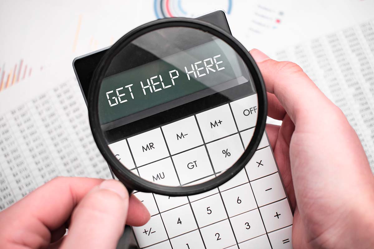  A black calculator on the screen, with the text "Get Help Here" magnified by a glass, against a backdrop of documents.