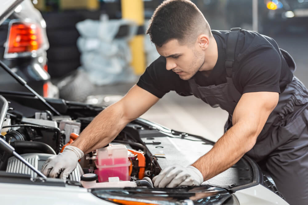 mechanic working under the hood of a car in a garage, representing car maintenance and registration loans as a financial option for vehicle-related expenses.