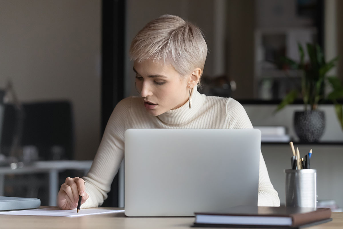 Female office worker typing on laptop at desk researching registration loans for emergencies