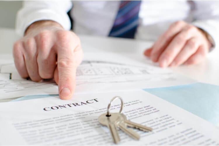 A contract for car title loans, with a key on top of it, and a finger pointing to the word 'contact' in the document.