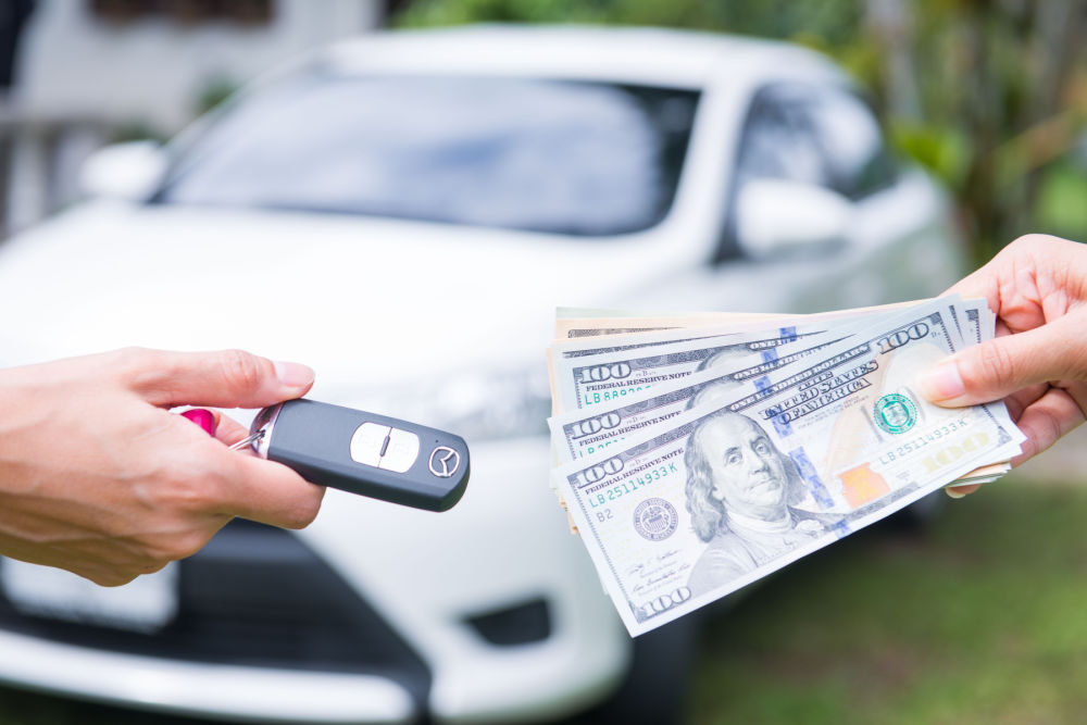 A car title loan cash negotiation between two people exchanging money and car keys, with a blurry background.