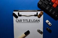 clipboard that has paper on it that reads car title loan next to keyboard and toy cars