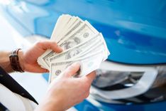 man counting title loan cash in front of his car