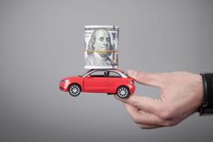 A hand holding a red toy car with title loan with cash on it roof