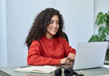 Woman with curly hair working on laptop at desk applying for signature installment loan.