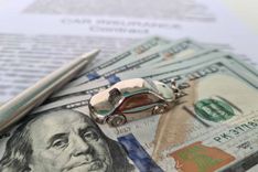 A close-up photo of a pile of hundred dollar bills and car keys, with papers related to registration loan in the background.