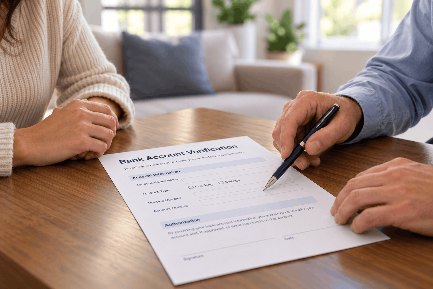 Two people reviewing a bank account verification form on a wooden table, with one pointing to the account information fields using a pen